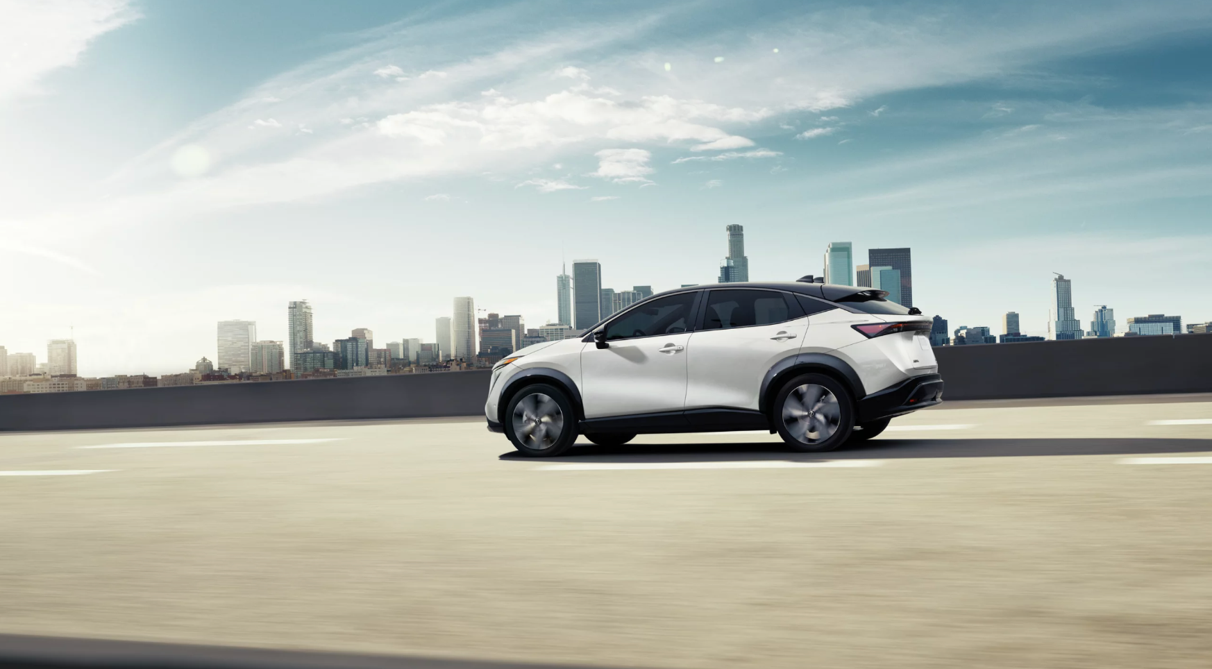 Profile view of a new Nissan Ariya parked in front of a city skyline